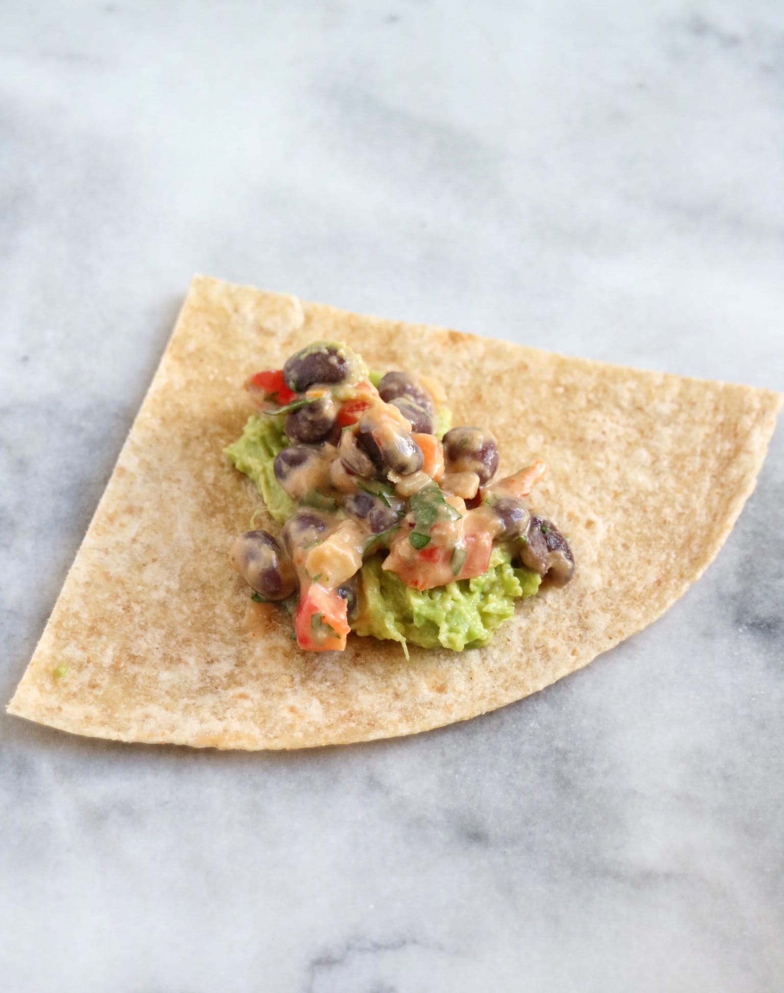 tortilla quarter with mashed avocado and bean filling on top | The Nutrition Adventure